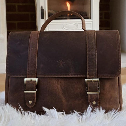 Postman Bag brown leather messenger bag displayed indoors by a fireplace