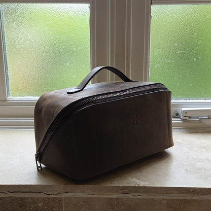 Side view of brown top grain crazy leather Toiletry Bag displayed by a window