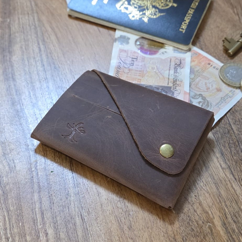 Brown top grain crazy leather Minimalist Wallet beside a passport, banknotes and coins on a wooden surface