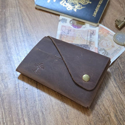 Brown top grain crazy leather Minimalist Wallet beside a passport, banknotes and coins on a wooden surface