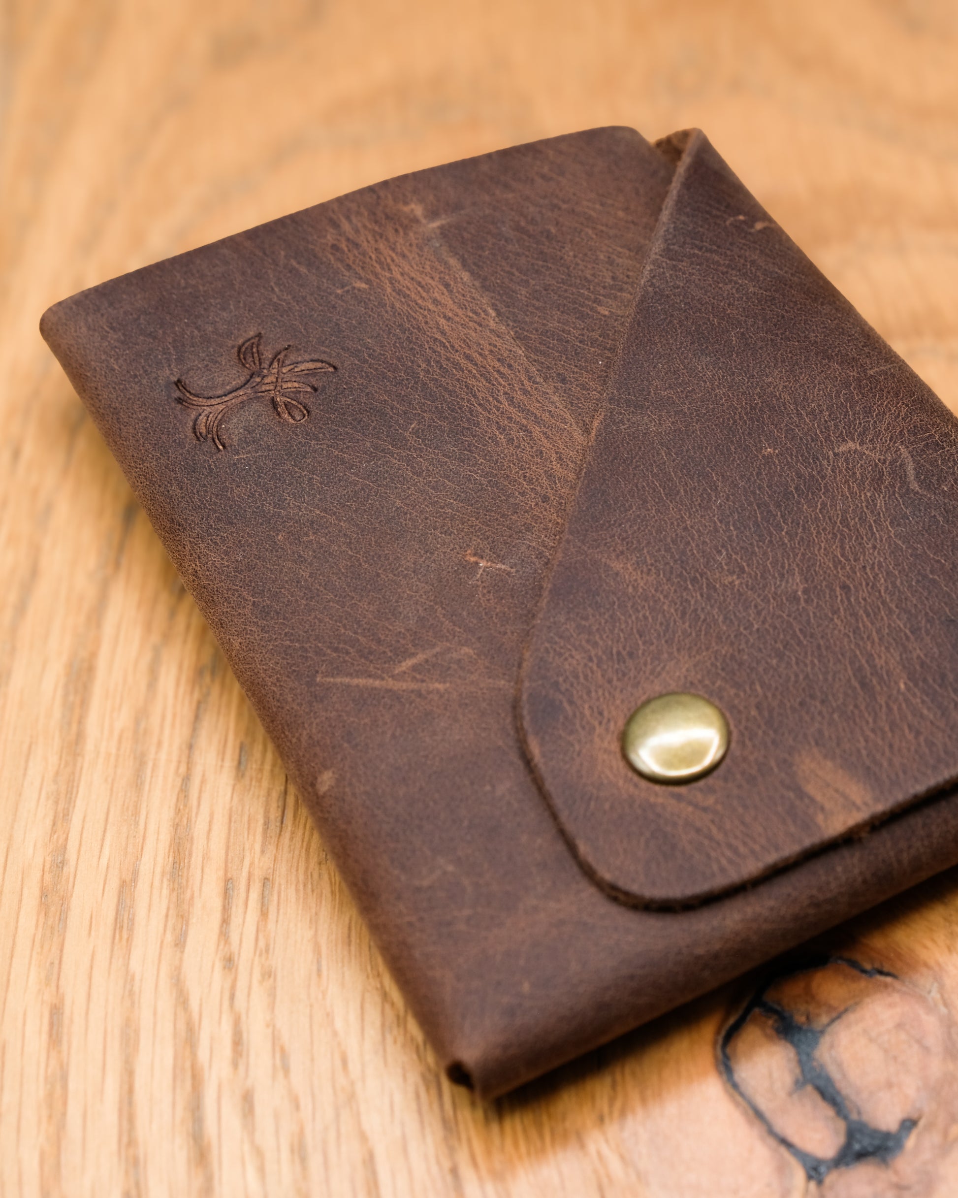 Close-up of brown top grain crazy leather Minimalist Wallet showing leather texture, embossed logo and brass snap closure
