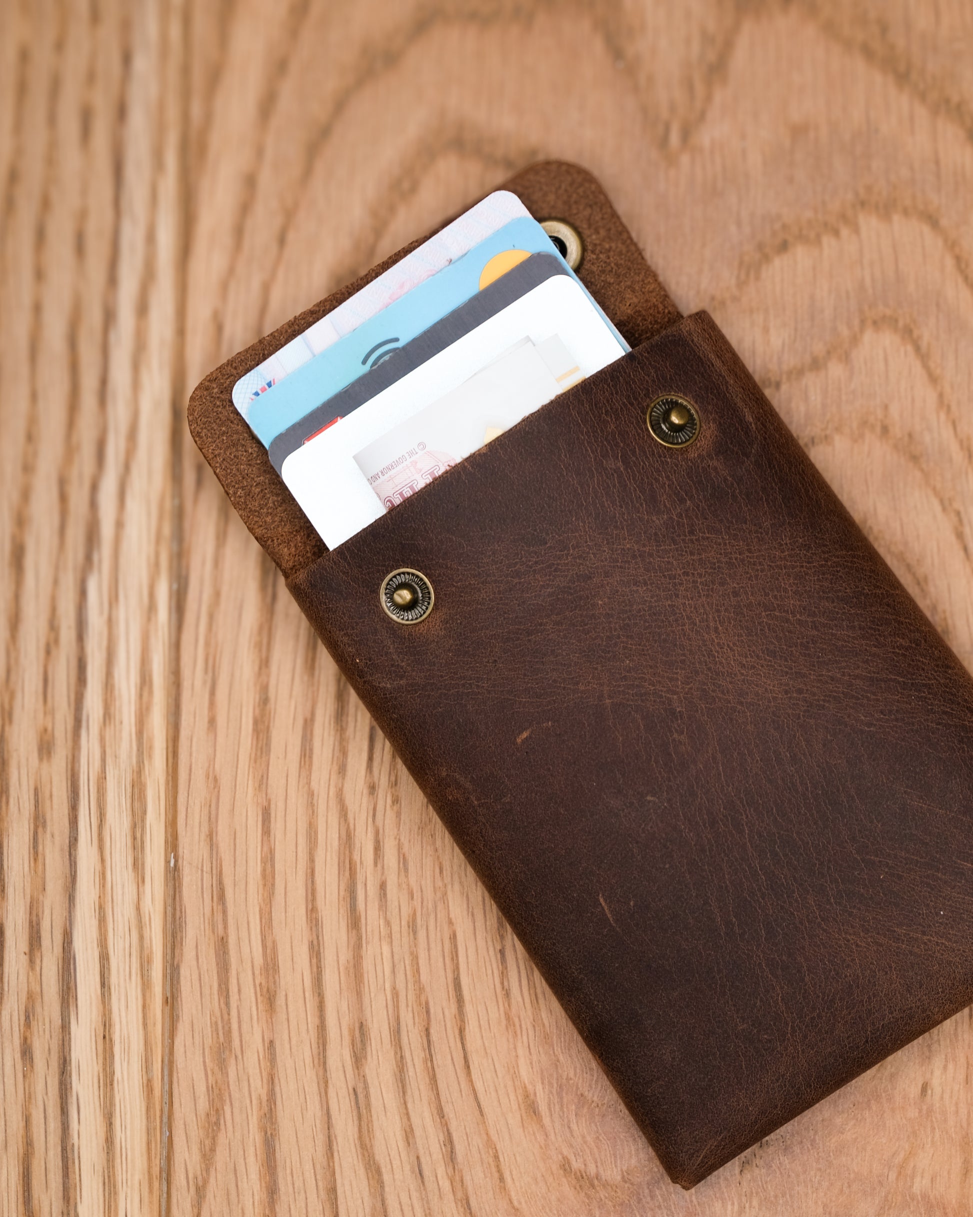 Open brown top grain crazy leather Minimalist Wallet holding cards on a wooden surface