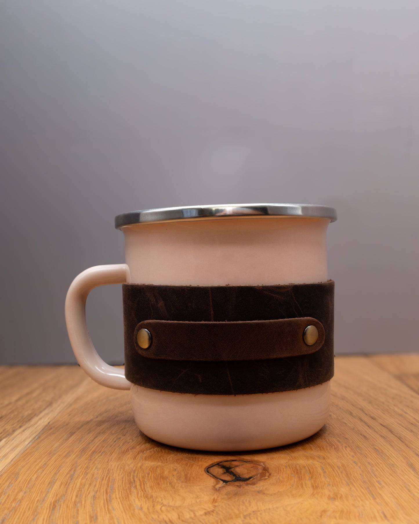 Pink enamel mug with a brown top grain crazy leather sleeve on a wooden surface