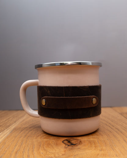 Pink enamel mug with a brown top grain crazy leather sleeve on a wooden surface