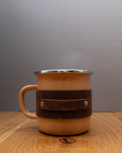 Brown enamel mug with a brown top grain crazy leather sleeve on a wooden surface