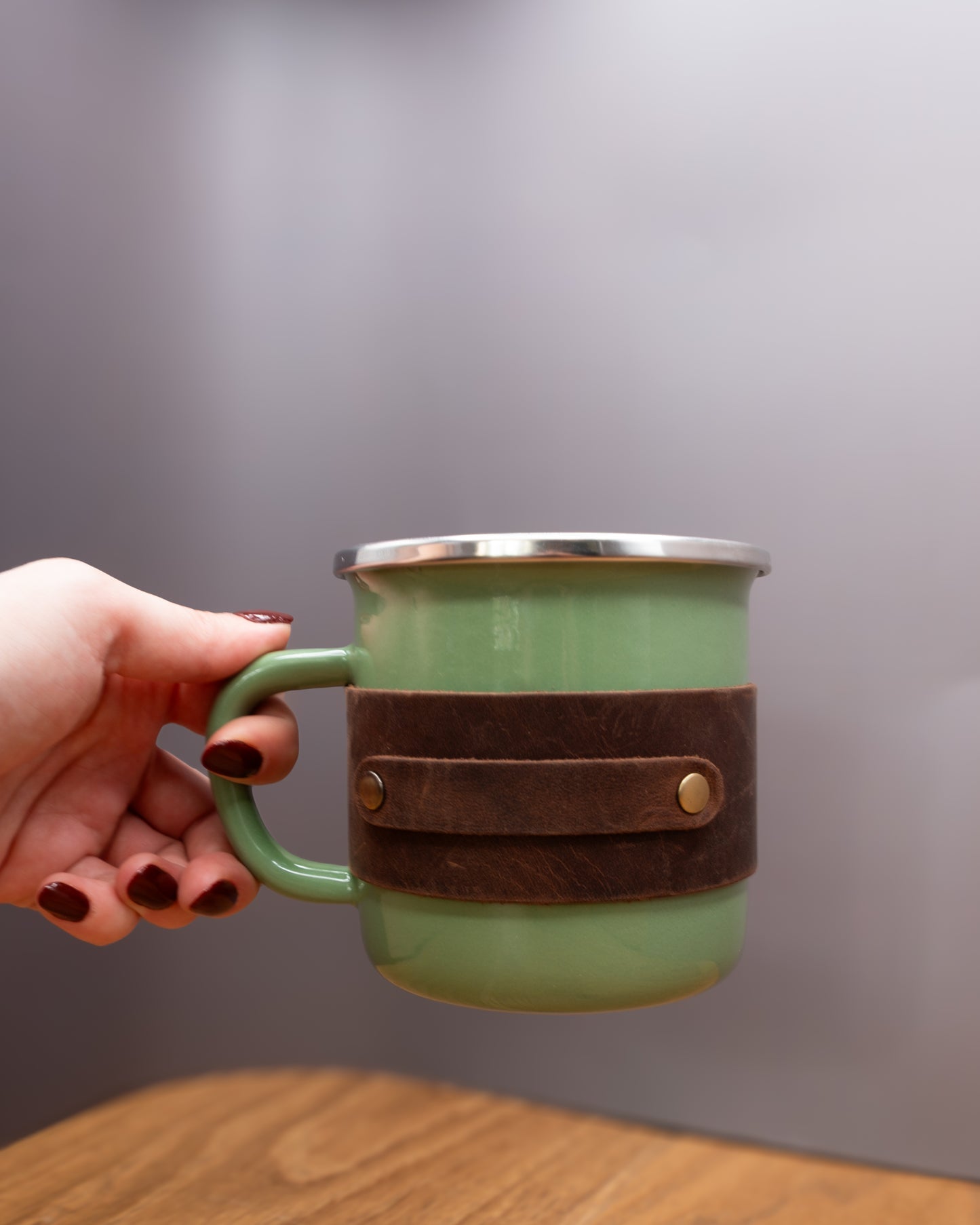 Green enamel mug with a brown top grain crazy  leather sleeve held by the handle