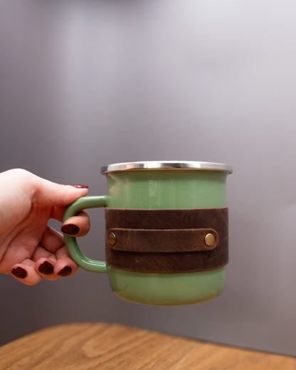 Green enamel mug with a brown top grain crazy  leather sleeve held by the handle