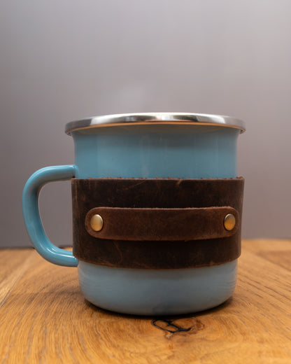Blue enamel mug with a brown top grain crazy leather sleeve on a wooden surface