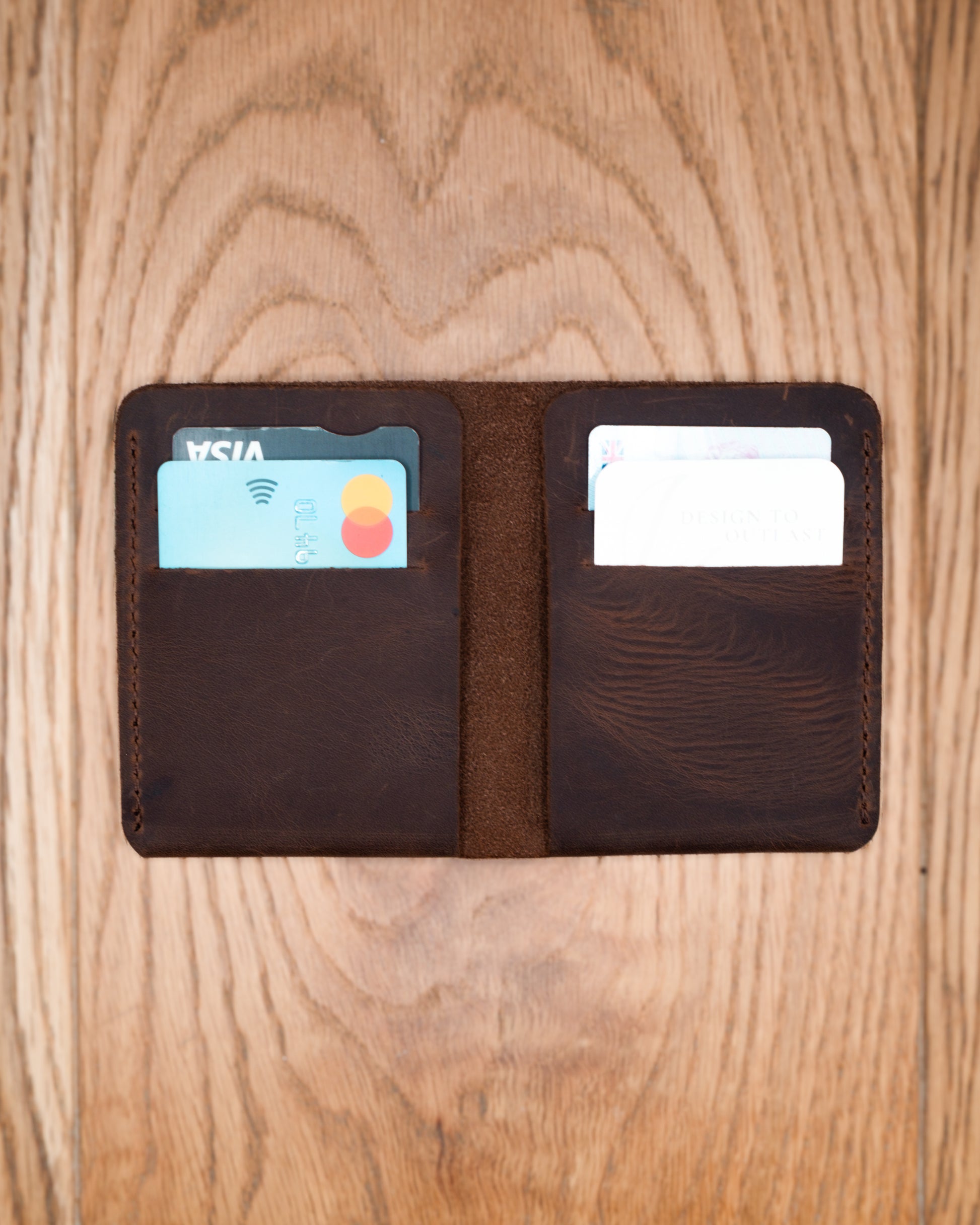 Open brown top grain crazy leather Card Holder holding cards in four interior card slots on a wooden surface