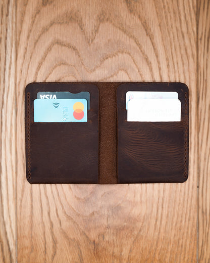 Open brown top grain crazy leather Card Holder holding cards in four interior card slots on a wooden surface