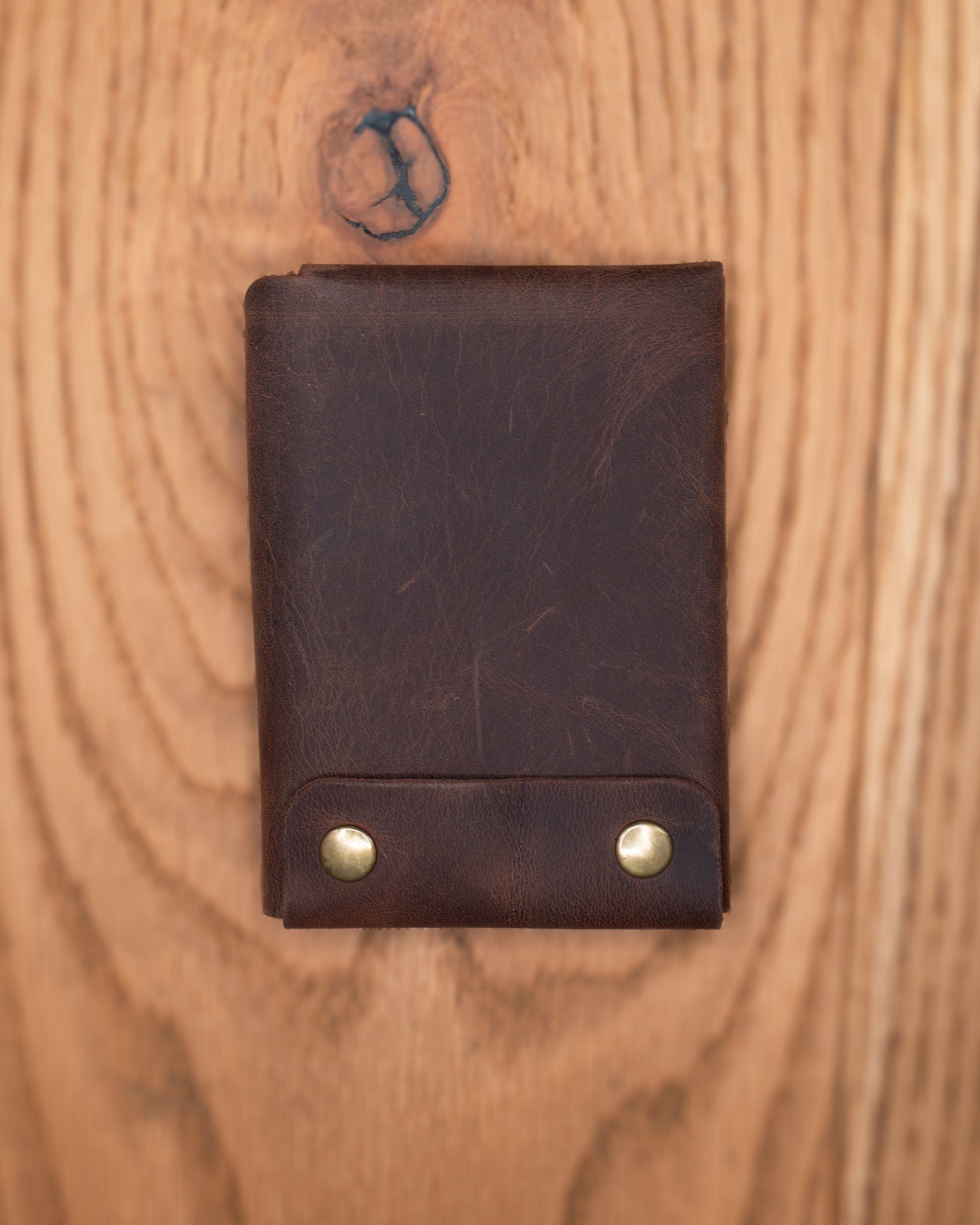 Back view of brown top grain crazy leather Minimalist Wallet with two brass rivets on a wooden surface