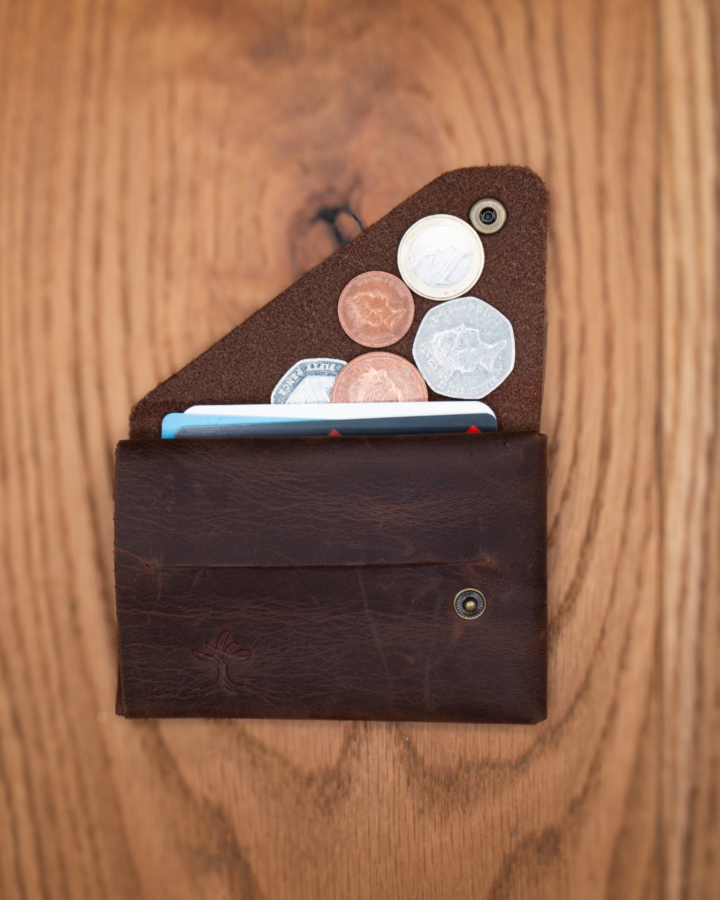 Open brown top grain crazy leather Minimalist Wallet holding cards and coins on a wooden surface